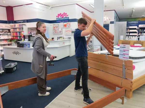 Zwei Personen bauen in einem Bettenfachgeschäft gemeinsam ein Holzbettgestell auf.