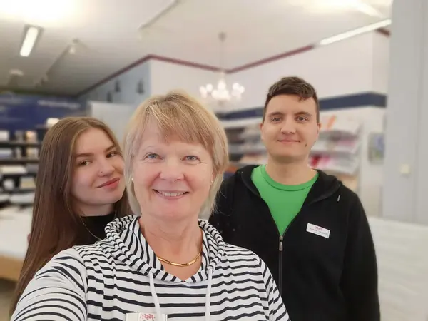 Drei freundliche Mitarbeitende stehen lächelnd in einem modernen Geschäft mit Regalen.