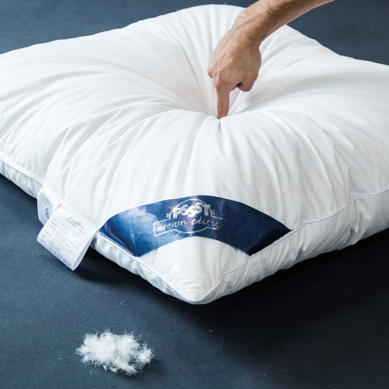 Hand drückt auf ein weiches Daunenkissen, das auf einem dunklen Untergrund liegt.